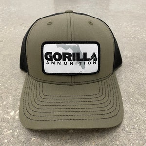 May include: A green and black trucker hat with a white patch that says "GORILLA AMMUNITION" and a black silhouette of a gorilla.