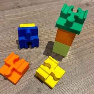 Könnte beinhalten: Vier farbige Plastikbausteine mit einem einzigartigen Verriegelungsdesign. Die Blöcke sind grün, orange, gelb und blau.
