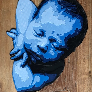 Op de afbeelding: Een blauw en zwart 3D-geprint beeldhouwwerk van een babygezicht.