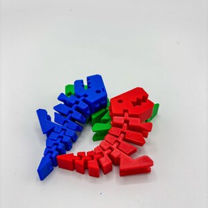 Op de afbeelding: Drie gelede dinosaurus skelet speelgoed in blauw, rood en groen. Het speelgoed is gemaakt van plastic en heeft een segmentontwerp, waardoor flexibele beweging mogelijk is. De achtergrond is effen wit.