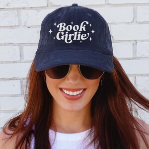 May include: Navy blue corduroy baseball cap with the text "Book Girlie" in white script and star accents. The hat is a classic six-panel design, perfect for book lovers and casual wear.