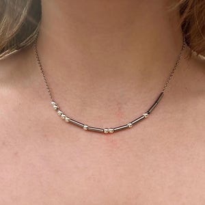 Puede incluir: Un collar de plata con una cadena y pequeñas barras de plata conectadas por pequeñas cuentas de plata.