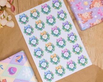 May include: A sheet of numbered wreath stickers with colorful bows, alongside two wrapped gifts. The gifts are wrapped in patterned paper with bows, reindeer, and geometric designs. A bouquet of flowers rests on the left, adding a touch of elegance to the scene.