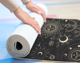 May include: A black yoga mat with a gold celestial design featuring suns, moons, and stars. The mat is rolled up and being held by a person's hands.