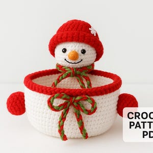 May include: A crocheted snowman-themed basket with a red rim and accents. The snowman has a red hat and a green and red scarf. The basket has two red side handles and a green and red bow. The text "CROCHET PATTERN PDF" is in the lower right corner.