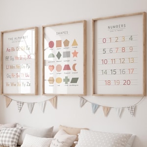 May include: Three framed educational posters with wooden frames hang on a white wall. The posters display the alphabet, shapes, and numbers from zero to twenty. A large woven giraffe and a wooden storage bench with pillows and storage bins are in the foreground.