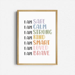 Op de afbeelding: Een ingelijste print met de woorden "I AM SAFE, CALM, STRONG, KIND, SMART, LOVED, BRAVE" in verschillende kleuren. De tekst staat in een eenvoudig, modern lettertype tegen een witte achtergrond. De lijst is lichtbruin.