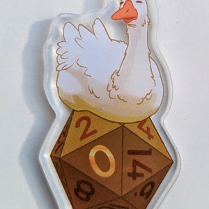 May include: A white goose with a red beak sits on top of a brown 20-sided die with gold accents. The die has the numbers 2, 0, 4, 17, 8, and 9 on its sides.