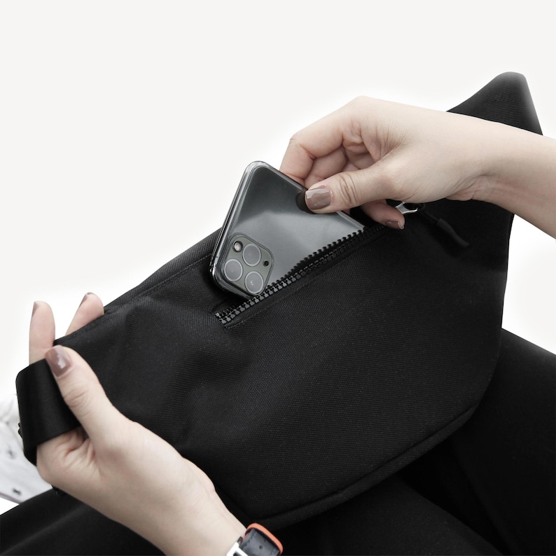 May include: A black zippered pouch with a black smartphone inside. The pouch has a zipper that is partially open.