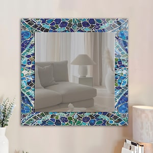 May include: Square mirror with a mosaic tile border in shades of blue, teal, and white. The mosaic design features irregular shapes and patterns, creating a decorative frame around the reflective surface. The mirror is a home decor item.