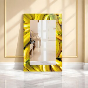 May include: A rectangular mirror with a vibrant banana-themed border. The frame is filled with a close-up of yellow bananas, creating a bright and playful design. The mirror reflects a room with a chair and white doors.