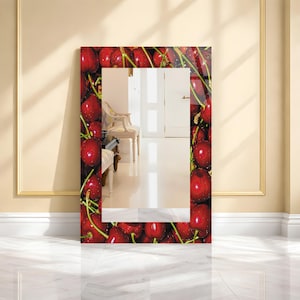 May include: A rectangular mirror with a vibrant border featuring a close-up of ripe red cherries. The mirror reflects a room with a white chair and doors. The frame is a glossy, decorative element.