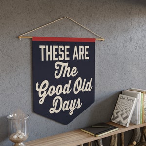 May include: A navy blue banner with white text that reads "These are the good old days". The banner is hanging from a wooden dowel rod with a red stripe at the top.