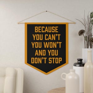 May include: A black and orange pennant banner with the text "Because you can't you won't and you don't stop" hanging on a white wall.