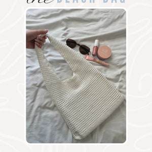 Puede incluir: Bolso de playa de crochet blanco con una parte superior ancha y abierta y una sola correa. El bolso est&aacute; sobre una colcha blanca con gafas de sol, brillo de labios y maquillaje en la superficie.