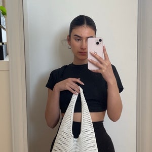 Puede incluir: Un bolso tote de crochet blanco con una camiseta negra de cuello alto y pantalones cortos negros.