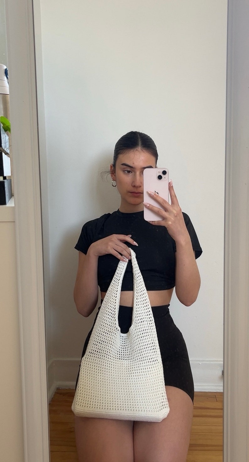 Puede incluir: Un bolso tote de crochet blanco con una camiseta negra de cuello alto y pantalones cortos negros.