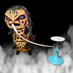 May include: A unique, hand-painted sculpture of a caterpillar-like creature with a hookah. The creature is yellow, brown, and green with blue eyes. The hookah is light blue with a white top and a white hose.