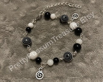 May include: Black and white beaded bracelet with a silver chain and a silver charm with a spiral design. The beads are round and have a swirl pattern.