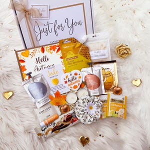 May include: A gift box labelled Just for You containing an autumn-themed card, a honey peel-off mask, a yellow jade pocket hug, a heart-shaped hello autumn ornament, two tea bags, a soap bar, a lip balm, a chocolate bar, and a floral scrunchie.
