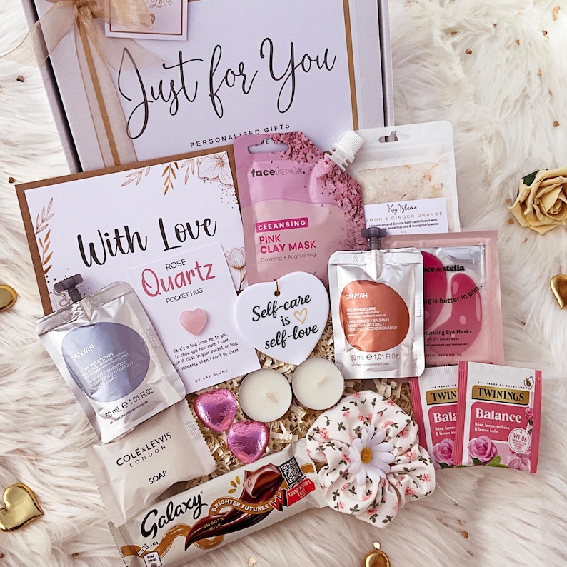 K&ouml;nnte beinhalten: Eine Geschenkbox mit der Aufschrift Just for You, die eine Face Facts rosa Tonmaske, einen Lanyah-Beutel, eine Rose Quartz Pocket Hug-Karte, ein herzf&ouml;rmiges Ornament mit der Aufschrift Self-care is self-love, zwei Teelichter, einen Galaxy-Riegel und Twinings-Tee enth&auml;lt.