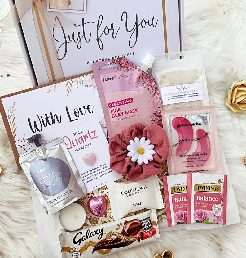 K&ouml;nnte beinhalten: Eine Geschenkbox mit einer Face Facts rosa Tonmaske, einem rosa Haargummi mit G&auml;nsebl&uuml;mchen, Grace & Stella Augenmasken, zwei Twinings Balance Teebeuteln, einem Galaxy Schokoriegel, einer Cole & Lewis Seife, einem Rosenquarz-Handschmeichler und 30 ml Shampoo.