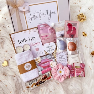 K&ouml;nnte beinhalten: Eine Geschenkbox mit der Aufschrift Just for You, die ein wei&szlig;es Handtuch, eine rosa Tonmaske, Augenmasken, Lippenbalsam, Seife, Twinings-Tee, einen Galaxy-Schokoriegel, ein rosa Haargummi mit G&auml;nsebl&uuml;mchen, zwei Teelichter und Karten mit Text enth&auml;lt.