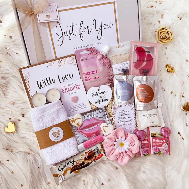 K&ouml;nnte beinhalten: Eine Geschenkbox mit der Aufschrift Just for You, die ein wei&szlig;es Handtuch, eine rosa Tonmaske, Augenmasken, Lippenbalsam, Seife, Twinings-Tee, einen Galaxy-Schokoriegel, ein rosa Haargummi mit G&auml;nsebl&uuml;mchen, zwei Teelichter und Karten mit Text enth&auml;lt.