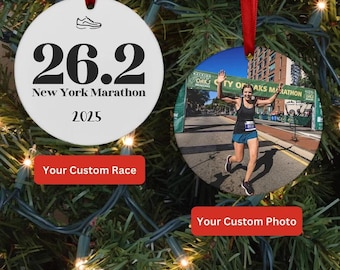 May include: Two round Christmas ornaments hanging on a green garland. One ornament features the text "26.2 New York Marathon 2025" and a running shoe icon. The other ornament displays a photo of a marathon runner. Both have red ribbons.