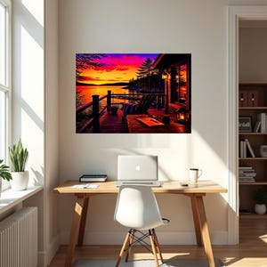May include: A wall art print depicting a wooden deck at sunset overlooking a calm lake. The scene features a dark wooden chair, a small table with a book and a lantern, and a vibrant sky with shades of orange, pink, and purple above the horizon.