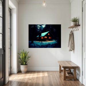 Op de afbeelding: Een rechthoekige wandkunstprint met een donkere hut in een besneeuwd bos bij nacht. De hut straalt een warm oranje licht uit vanuit de ramen en de deur, wat contrasteert met de diepblauwe tinten van de omringende bomen en de sneeuw.