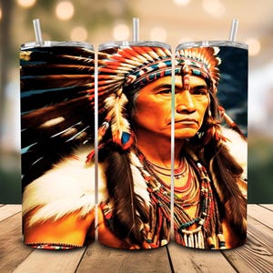 Op de afbeelding: Drie roestvrijstalen bekers met een portret van een inheemse Amerikaan. Het ontwerp toont een persoon met een gevederde hoofdtooi, kettingen en een bontkraag. De bekers hebben doorzichtige rietjes. De achtergrond is wazig.