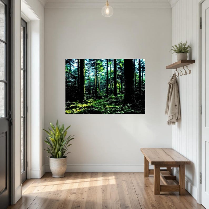 May include: A rectangular wall art print featuring a dense forest scene with tall dark tree trunks and vibrant green mossy ground. The artwork is displayed on a plain white wall in a hallway, positioned above a wooden bench and a potted plant.