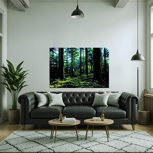May include: A rectangular wall art print featuring a dense forest scene with tall dark tree trunks and vibrant green foliage illuminated by sunlight, displayed in a living room above a black tufted leather sofa with two round wooden tables.
