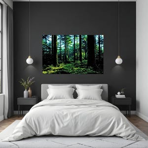 May include: A rectangular wall art print featuring a dense forest scene with tall dark tree trunks and vibrant green mossy ground, displayed above a bed with white bedding, two black nightstands, and two hanging pendant lights.