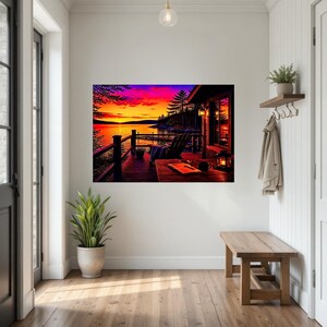 May include: A rectangular wall art print depicting a sunset over a lake viewed from a wooden deck. The scene features a dark silhouette of a chair, a table with a book and a lantern, and a vibrant sky with shades of orange, pink, and purple.