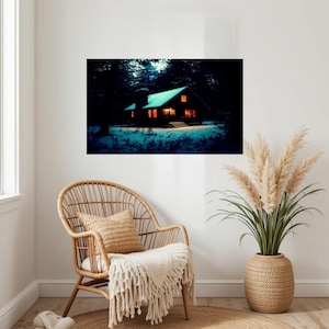 Op de afbeelding: Een rechthoekige wandkunstprint met een donkere hut in een besneeuwd bos bij nacht. De hut heeft een gloeiend dak en warm oranje licht dat uit de ramen straalt, wat contrasteert met de diepblauwe tinten van de omringende bomen en sneeuw.