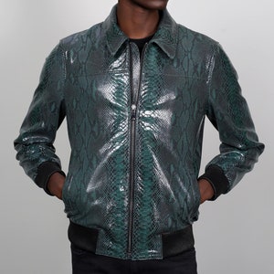 Może przedstawiać: Zielona kurtka bomberowa ze skóry węża z zamkiem błyskawicznym. Kurtka ma żebrowany kołnierz, mankiety i dół.