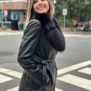 May include: A black leather jacket with a fur collar and a belt. The jacket has a long sleeve and a front zipper closure.