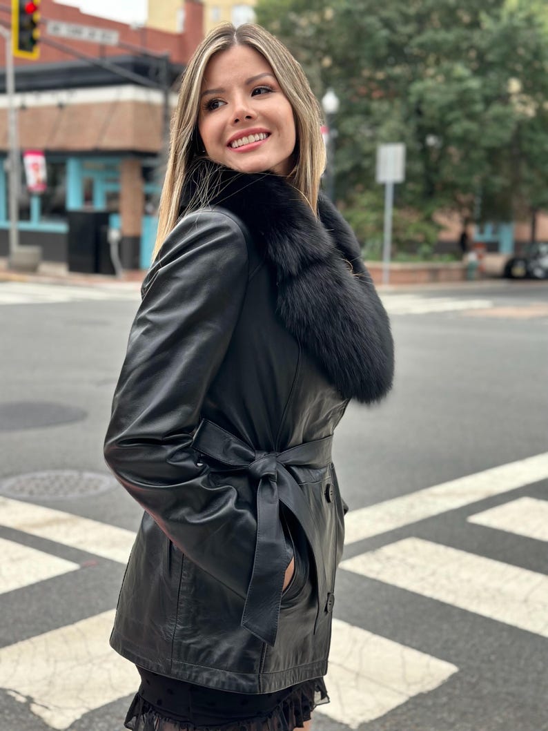May include: A black leather jacket with a fur collar and a belt. The jacket has a long sleeve and a front zipper closure.