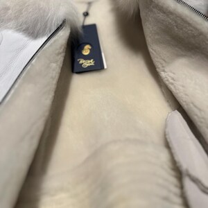 Op de afbeelding: Witte shearlingjas met een witte bontkraag en een ritssluiting. De jas is gevoerd met wit shearling en heeft een label met de tekst "Boyd".