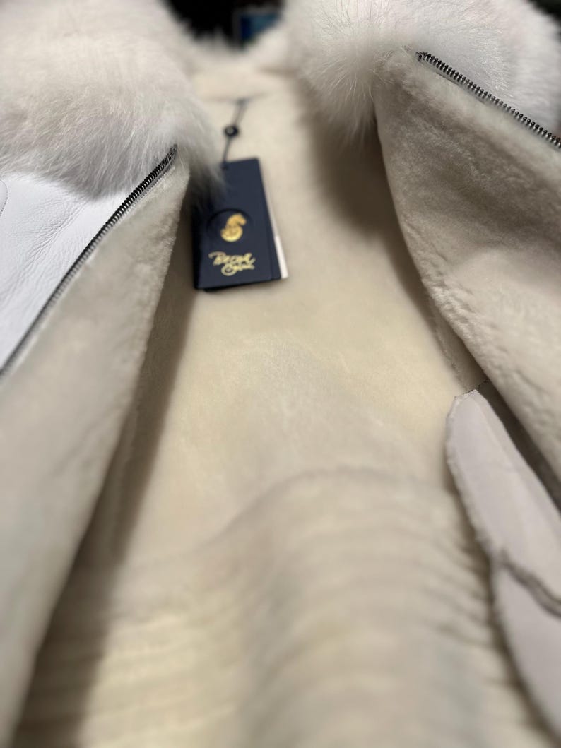 Op de afbeelding: Witte shearlingjas met een witte bontkraag en een ritssluiting. De jas is gevoerd met wit shearling en heeft een label met de tekst "Boyd".