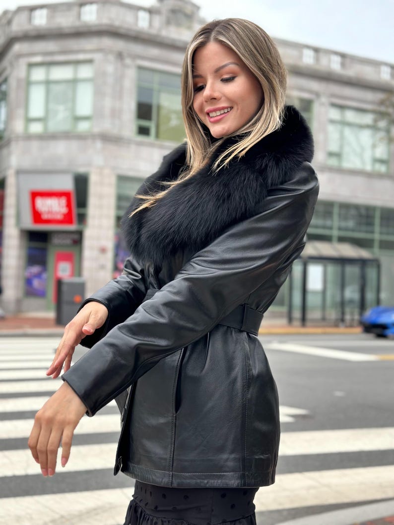 May include: A black leather jacket with a large black fur collar. The jacket has a belt and is cinched at the waist.