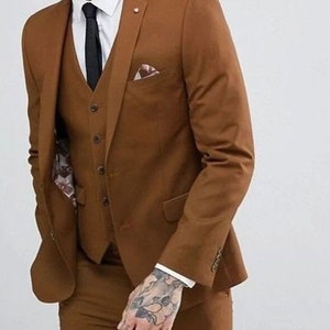 May include: A brown three-piece suit with a white shirt and a black tie. The suit jacket has a pocket square.
