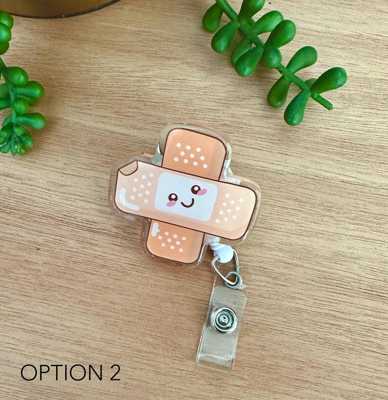 May include: A clear plastic badge holder with a cute cartoon bandage design. The bandage is orange and has a smiling face with pink cheeks. The badge holder has a retractable cord and a clip.