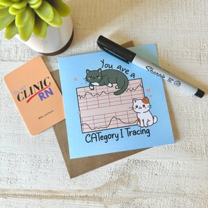 May include: A blue card with the text "You are a Category I Tracing" and a cartoon image of two cats. One cat is black and green and the other is white with orange spots. The card is sitting on a brown surface.
