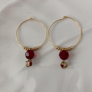 May include: Gold hoop earrings with a dangling red faceted bead and a smaller gold bead.