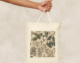 Op de afbeelding: Een beige canvas tote bag met een bloemenprint met groene bladeren en witte bloemen. De print is een vintage botanische illustratie.