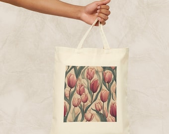 Op de afbeelding: Een witte canvas tote bag met een roze en groene bloemenprint van tulpen. De tas heeft twee lange hengsels.