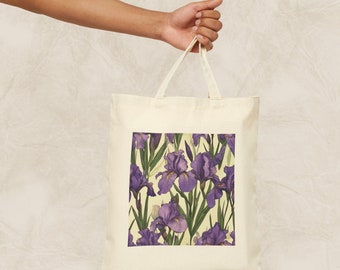 Op de afbeelding: Een witte canvas tote bag met een print van paarse irissen. De tas heeft twee lange hengsels.